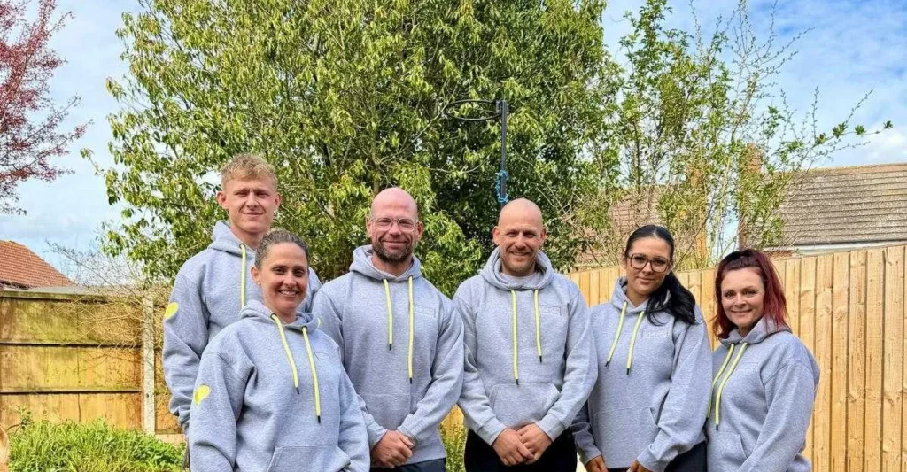 The Empowered Minds team — six mentors and coaches in Empowered Minds branded hoodies, photographed in a garden